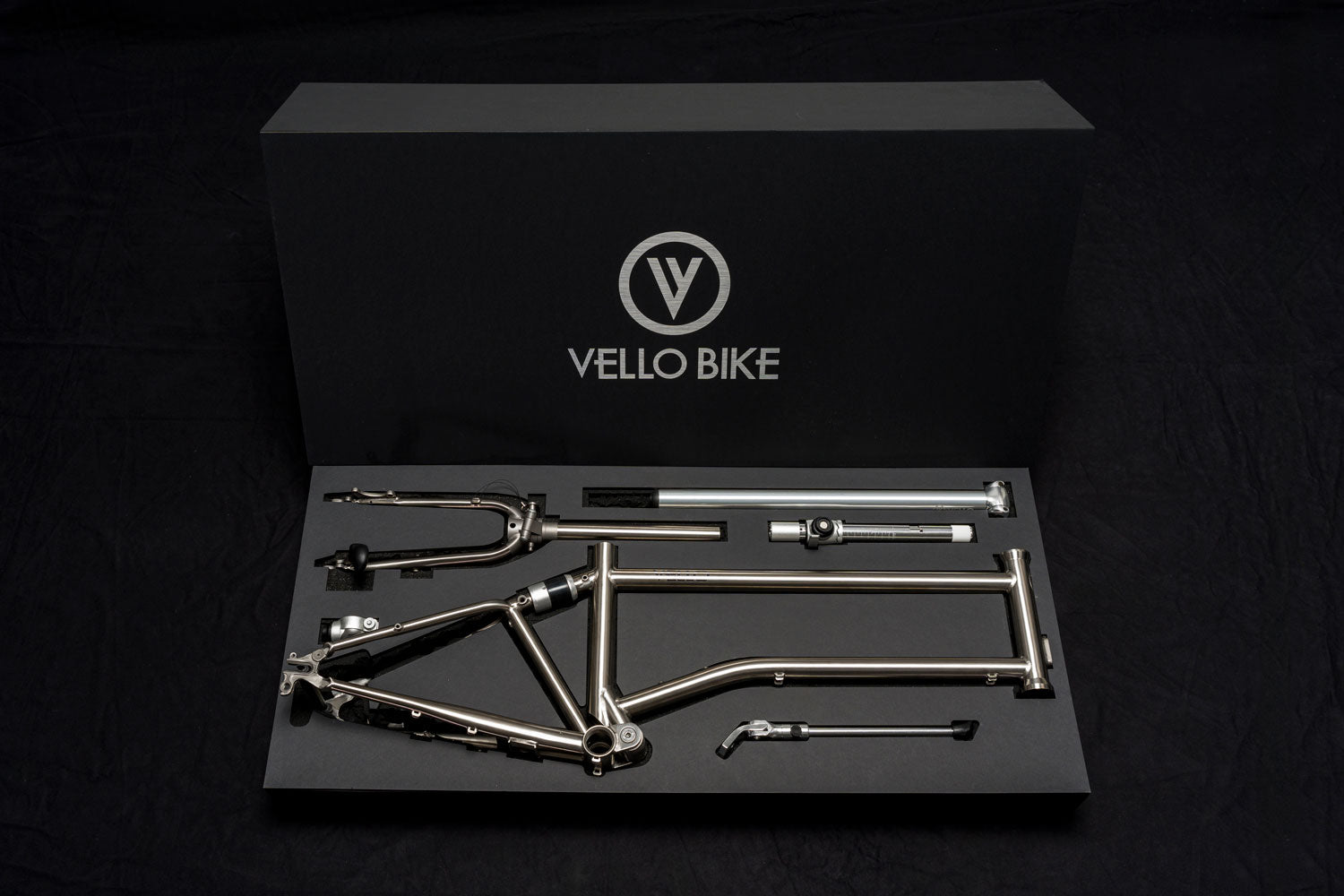 Das limitierte Titanrahmenset von VELLO mit einer offenen schwarzen Box auf der das Logo ganz groß hinterlegt ist und die Fahrradteile alle schon ein geschlichtet sind.