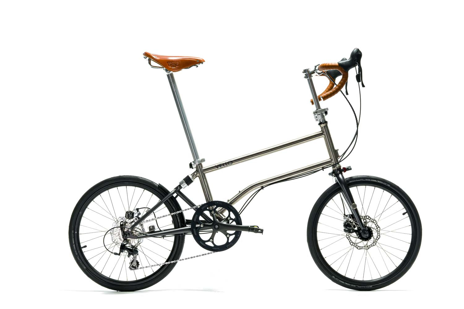 Ein entfaltetes VELLO Speedster Titan Faltrad / Klapprad ,in der Farbe gebürstetes Titan, mit 20 Zoll Schwalbe One Tube Type Performance 28-451 Reifen und dem ikonischen Honigbraunen Sattel, sowie Griffen.