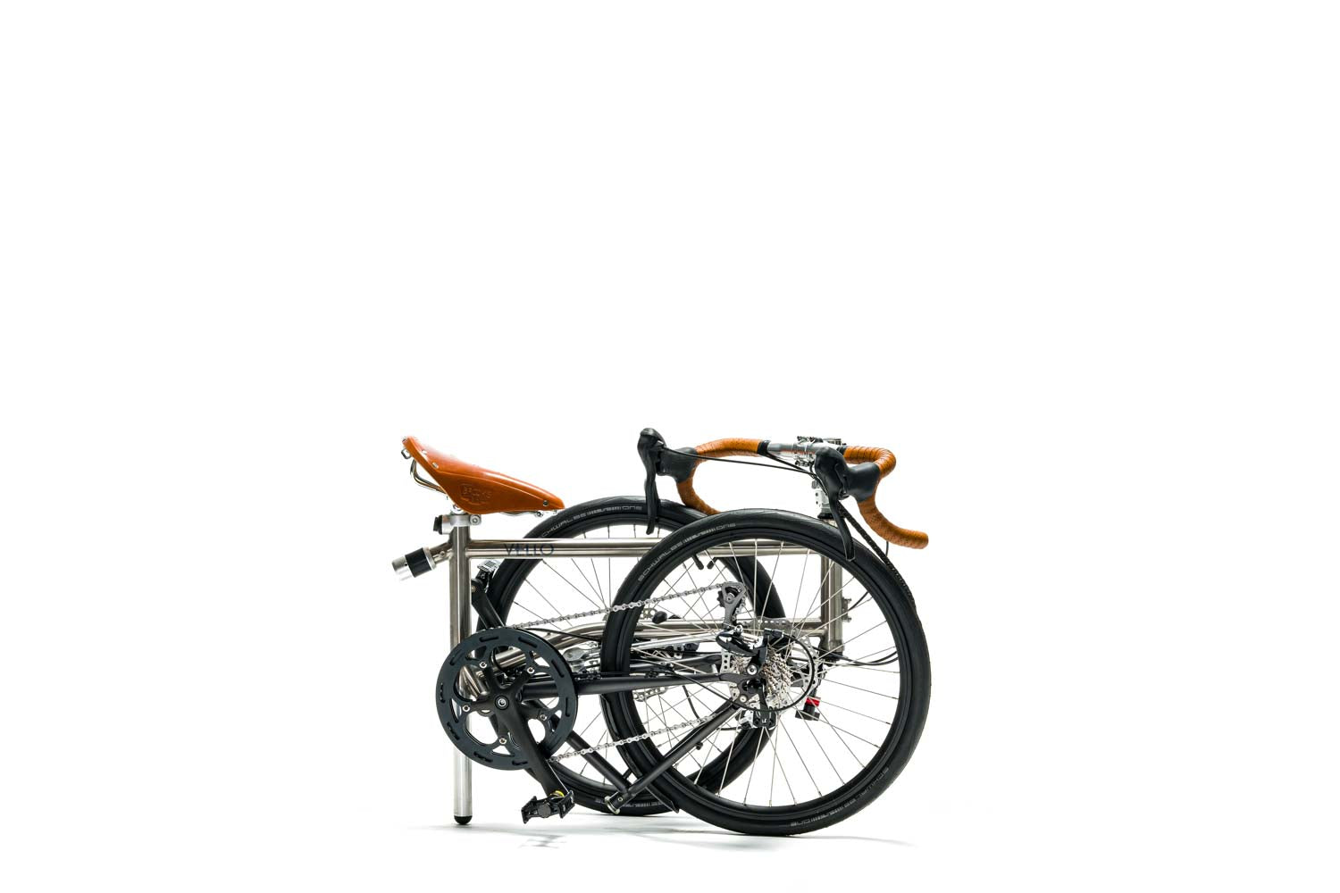 Ein gefaltetes VELLO Speedster Titan Faltrad / Klapprad ,in der Farbe gebürstetes Titan, mit 20 Zoll Schwalbe One Tube Type Performance 28-451 Reifen und den ikonischen Honigbrauenen Sattel, sowie Griffen.