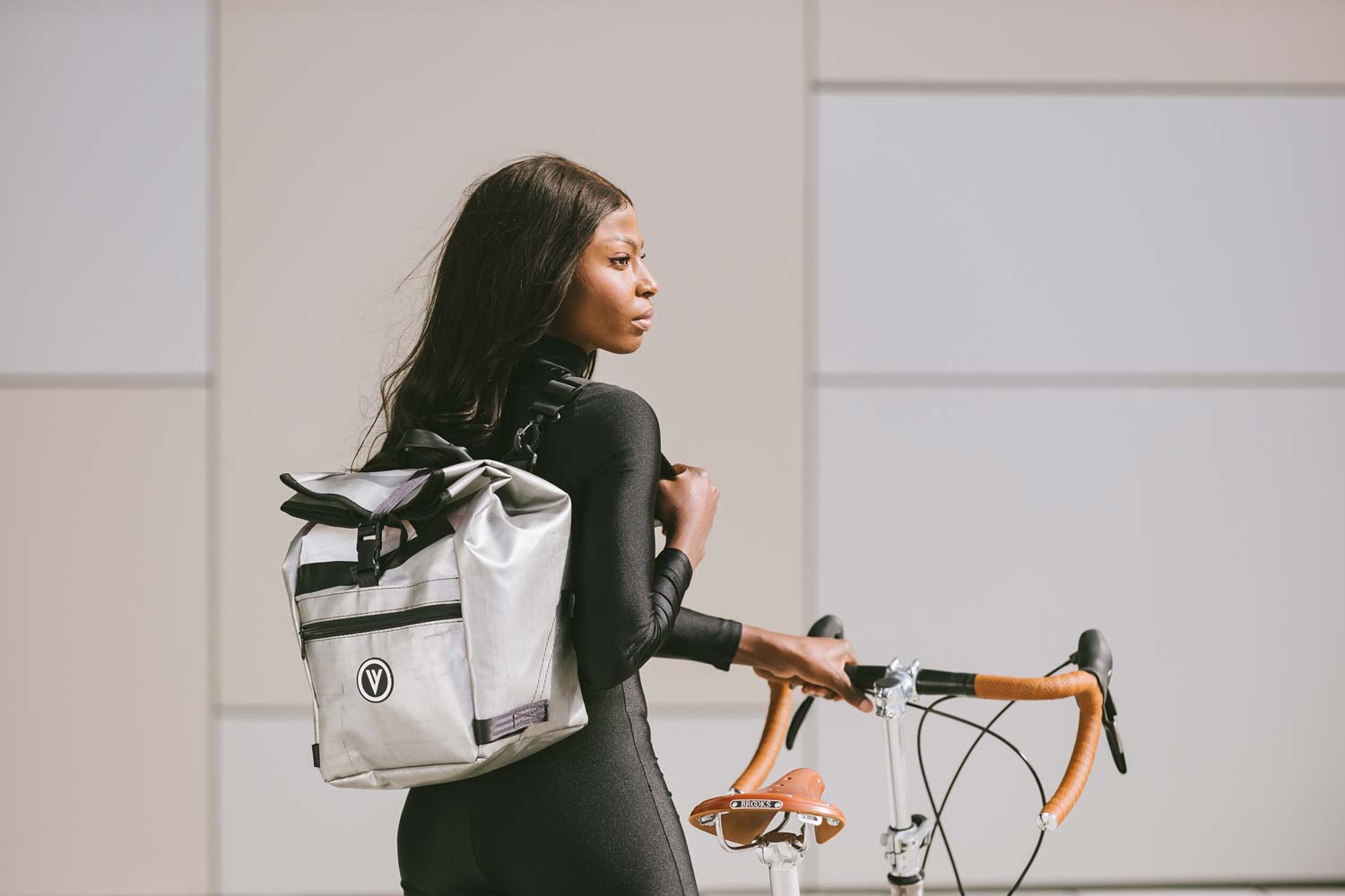 Eine Frau mit einem VELLO Speedster Titan Faltrad / Klapprad in der Farbe gebürstetes Titan, mit 20 Zoll One Tube Type Performance 28-451 Reifen und mit einem weißem Daypack im Gepäckträger.