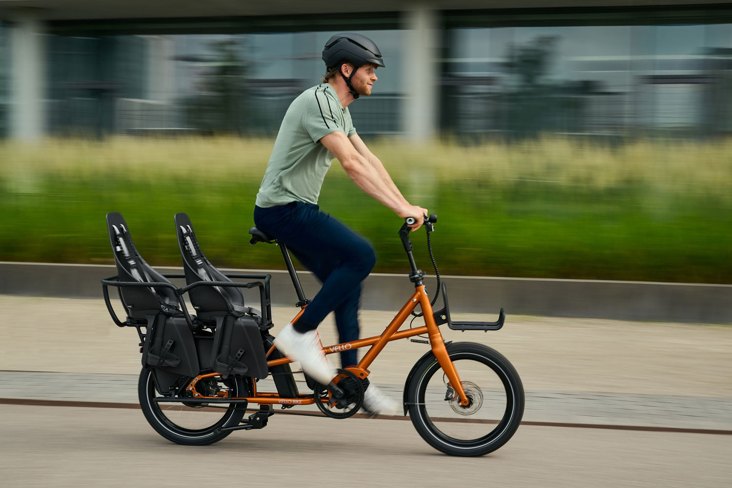 Ein Mann fahrt auf einem VELLO SUB mit 2 Urban IKI MIK HD Kindersitzen und dem Cool Kid Reling durch die Stadt.