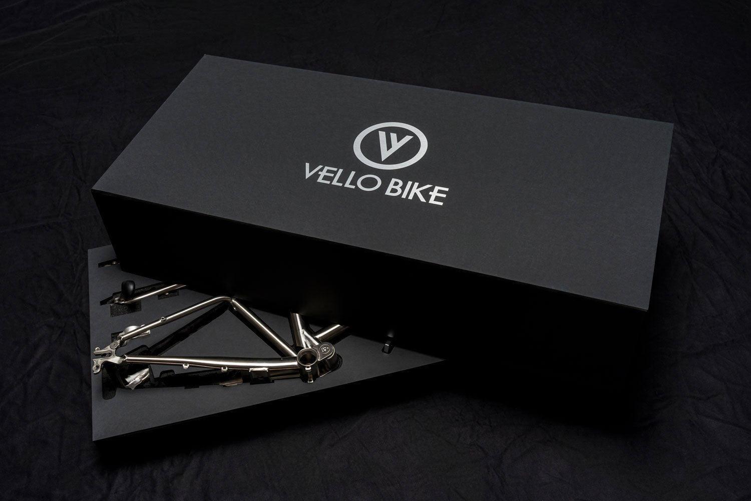 Das limitierte Titanrahmenset von VELLO mit einer halboffenen schwarzen Box auf der das Logo ganz groß hinterlegt ist und die ein mysteriöses Gefühl erweckt.
