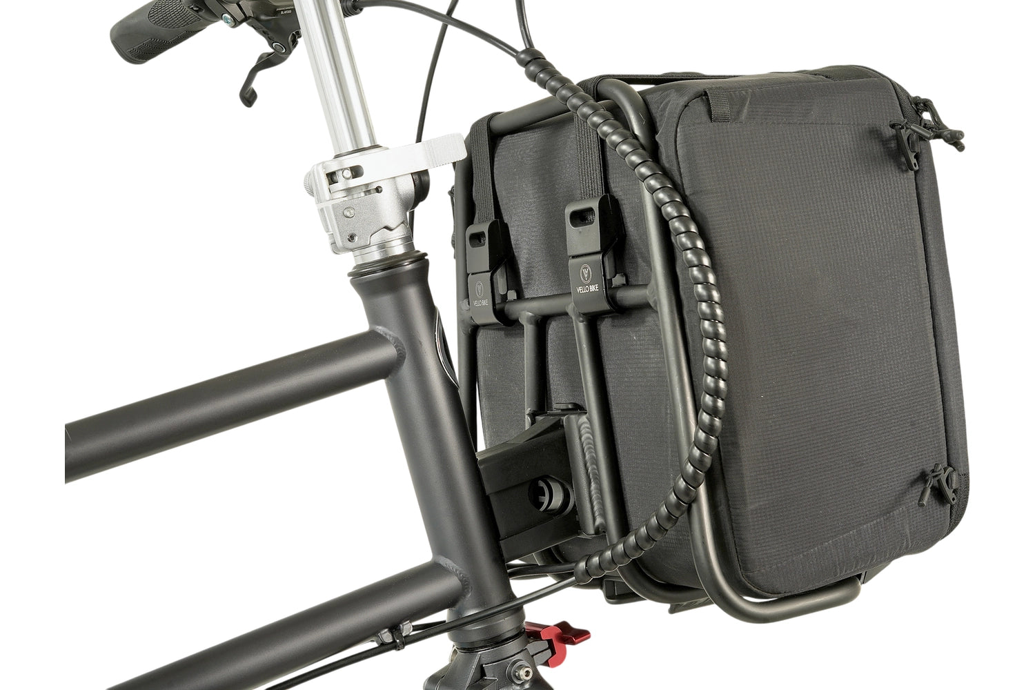 Eine schwarze würfelförmige Tasche ist mit 2 VELLO HD Spanngurten an einem VELLO Pizza Rack, der wiederum an einem VELLO Faltrad montiert ist, befestigt. Ansicht von seitlich-hinten. 