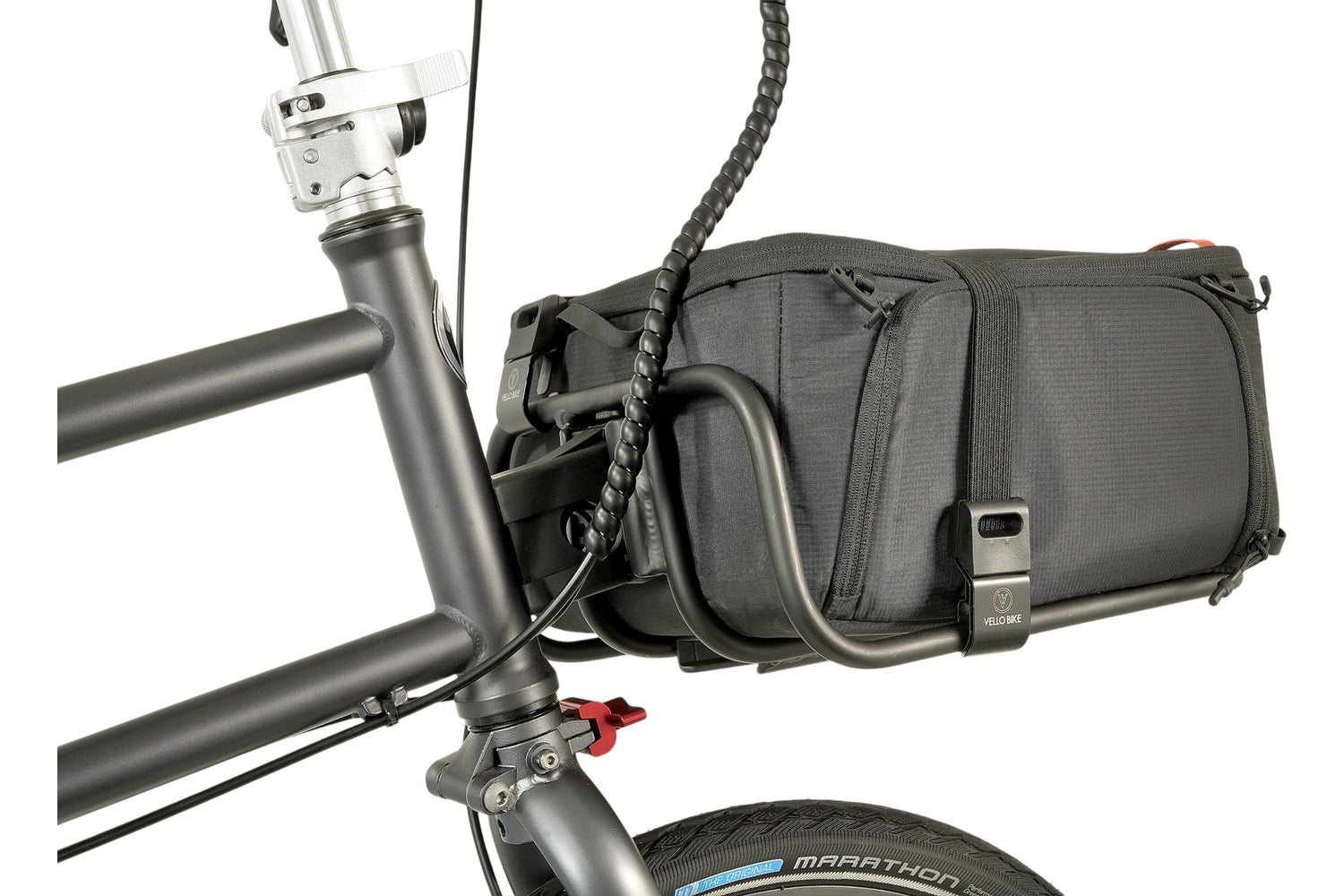 Eine schwarze quadratische Tasche ist mit 2 VELLO HD Spanngurten an einem VELLO Pizza Rack, der wiederum an einem VELLO Faltrad montiert ist, befestigt. Ansicht von seitlich-hinten. 